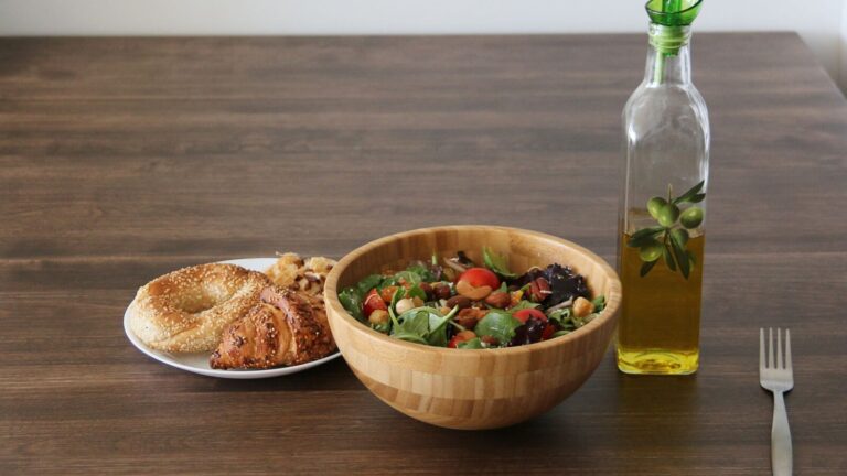 Bol de salade, huile d'olive et fruits secs posés sur une table en bois