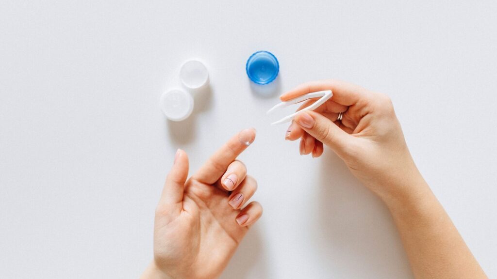Mains manipulant un étui à lentilles de contact au-dessus d'un plan blanc
