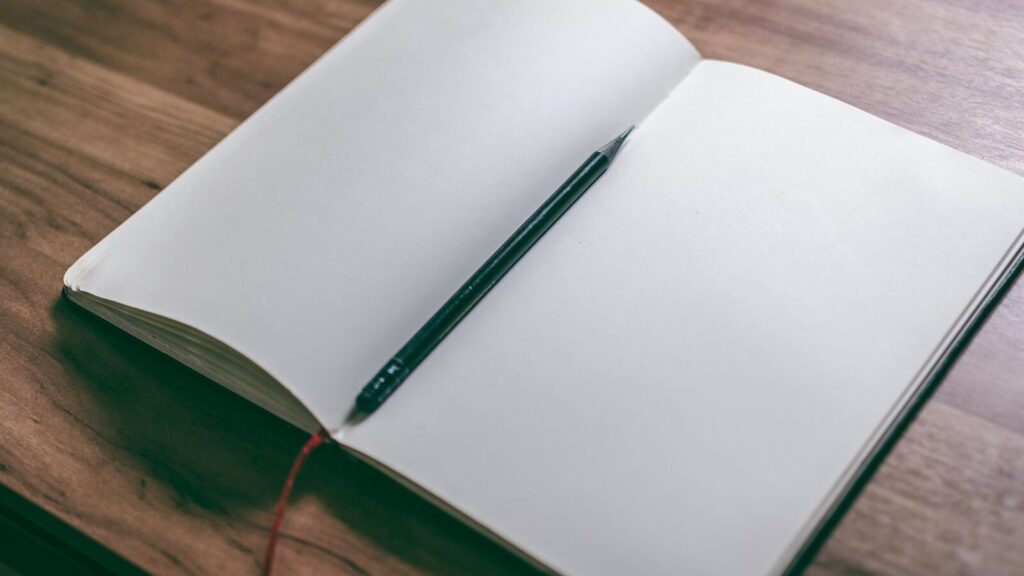 Carnet ouvert sur une table en bois avec un crayon posé en travers
