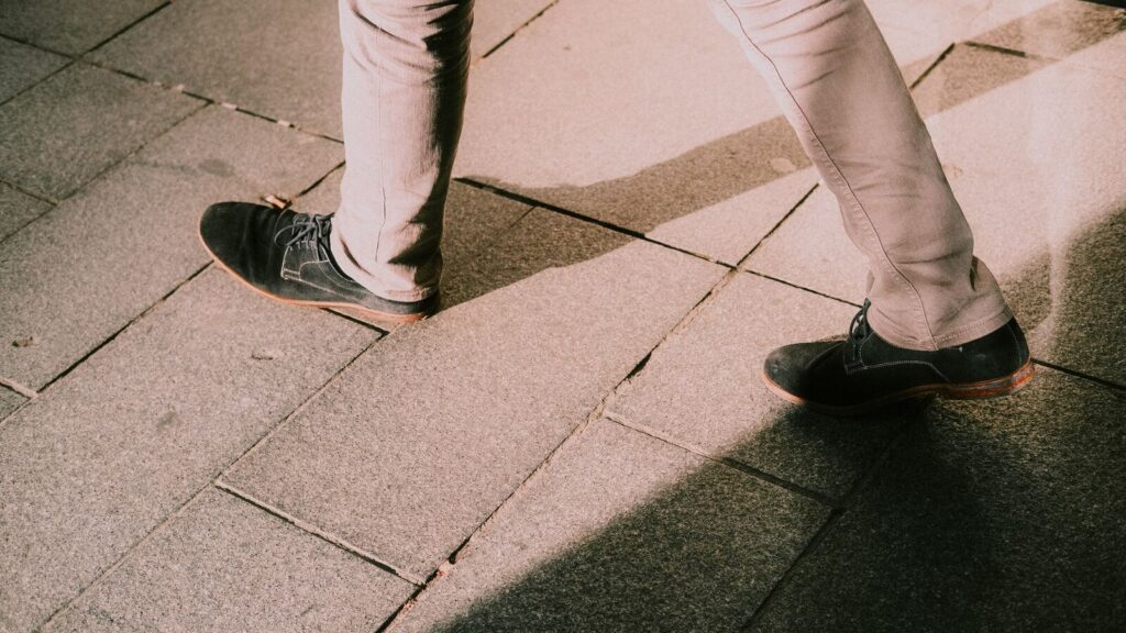 Jambes et chaussures noires marchant sur un pavage de pierre en ville