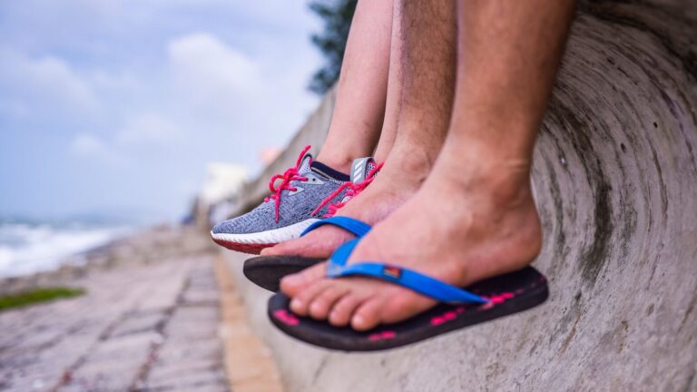 Pieds en baskets et en tongs posés côte à côte sur un muret au bord de mer
